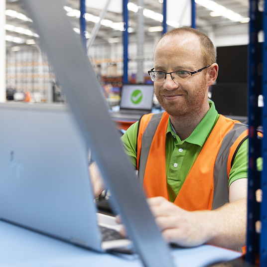 One of Stock Must Go employees testing a laptop. He has ginger hair and is wearing glasses, he has a smile on his face.